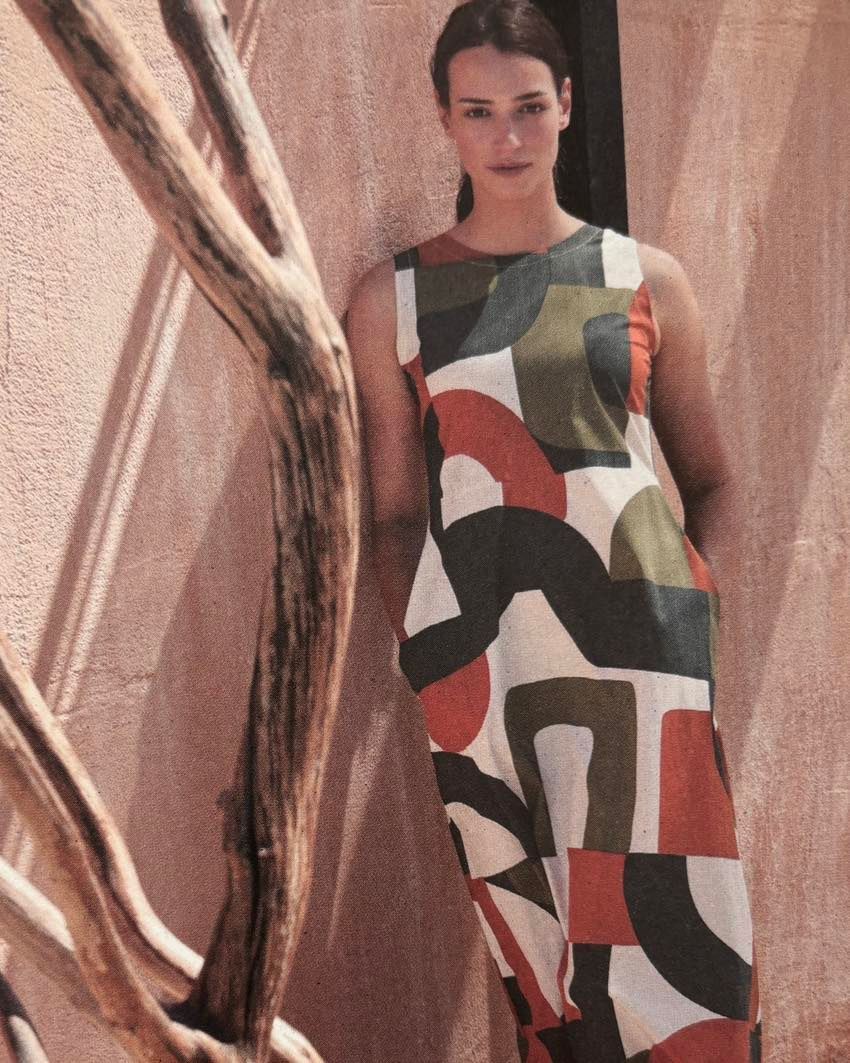 Una donna con un vestito colorato è in piedi accanto a un albero