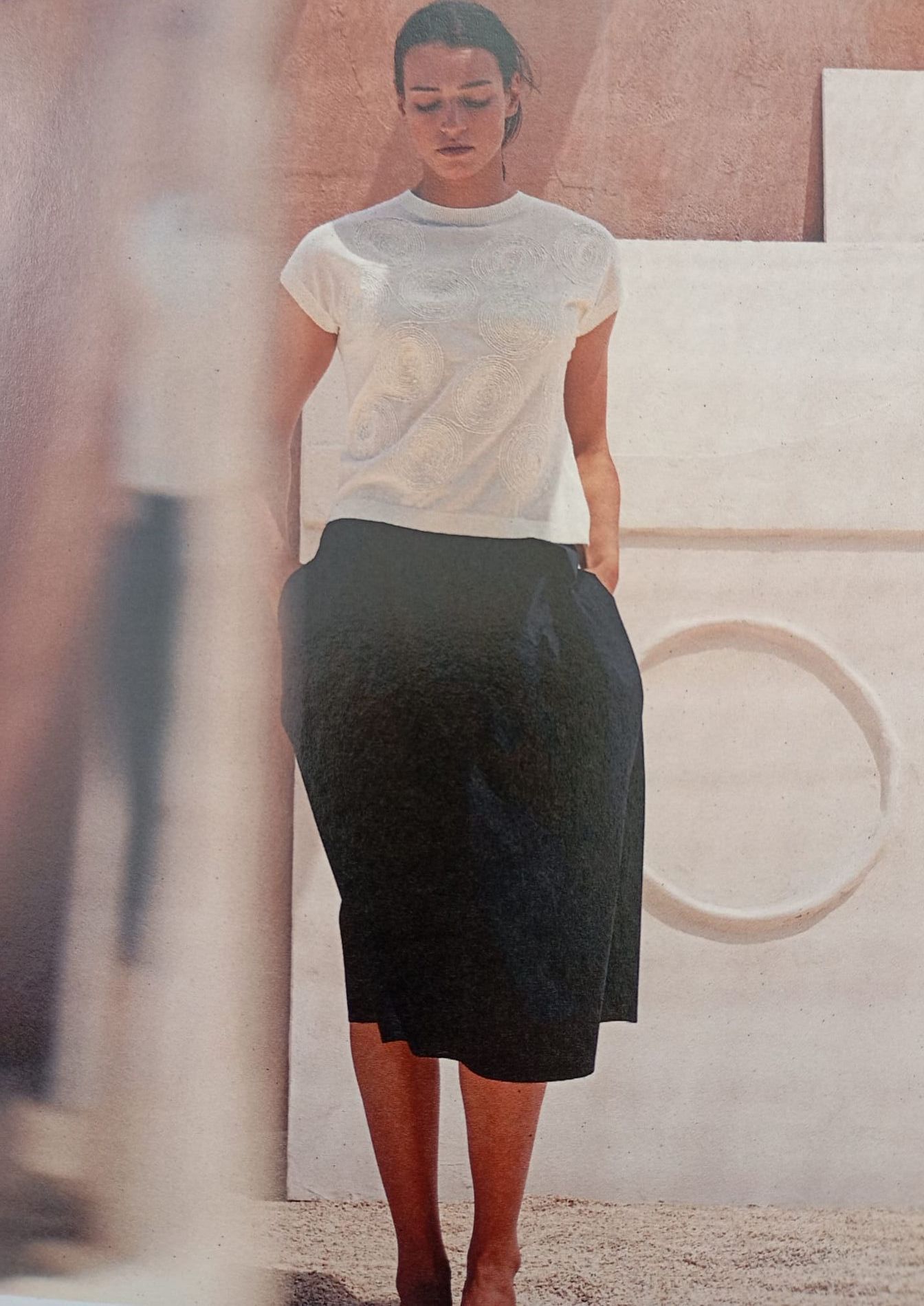 Una donna con una camicia bianca e una gonna nera è in piedi davanti a un muro bianco