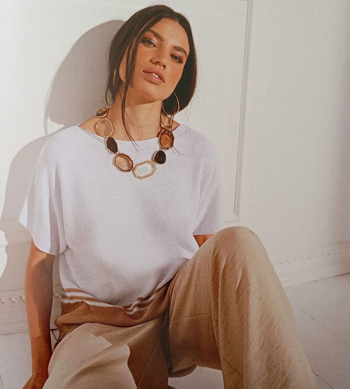 Una donna che indossa una camicia bianca e pantaloni color cuoio è seduta sul pavimento.