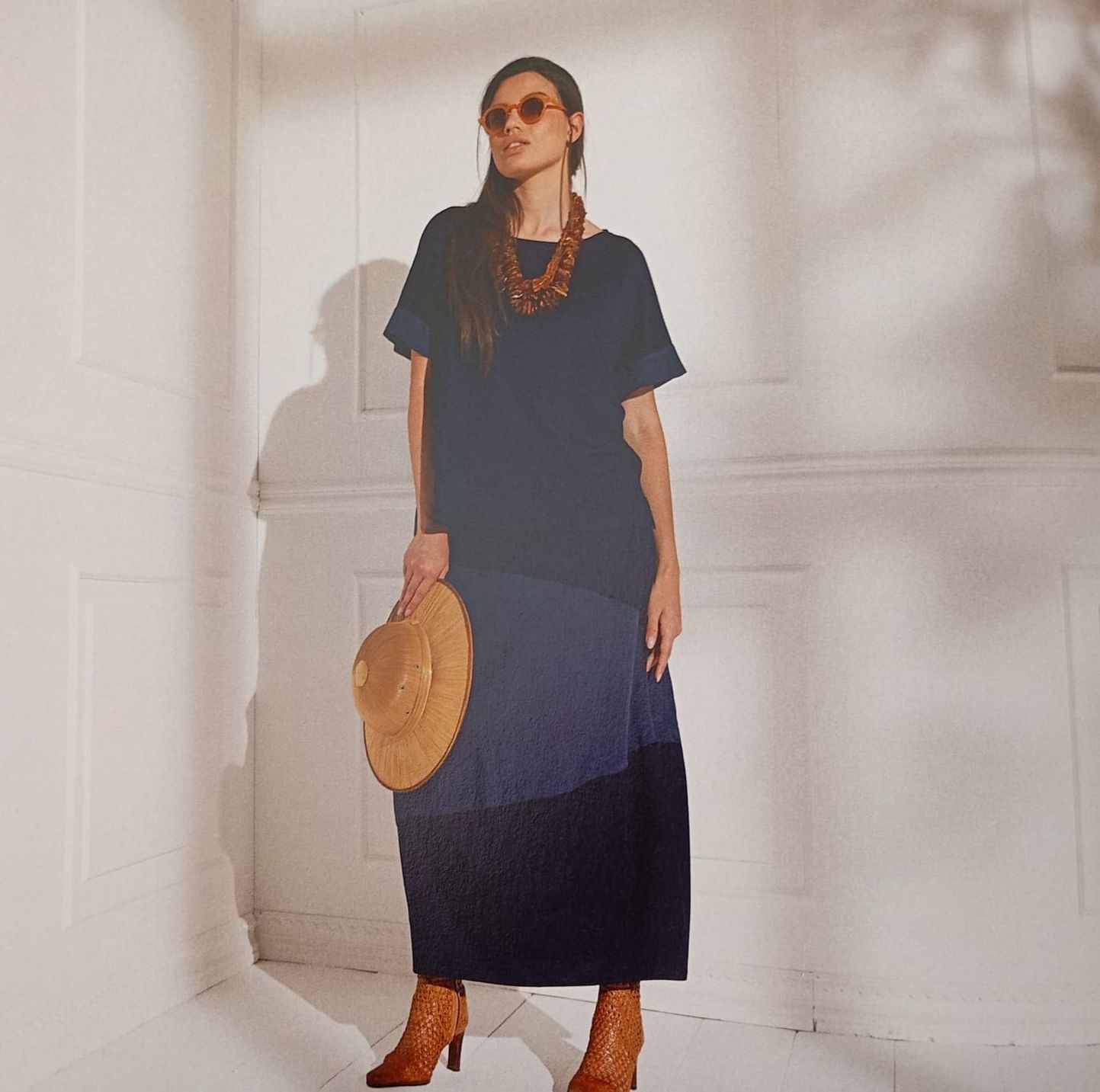 Una donna in un vestito blu tiene in mano un cappello di paglia