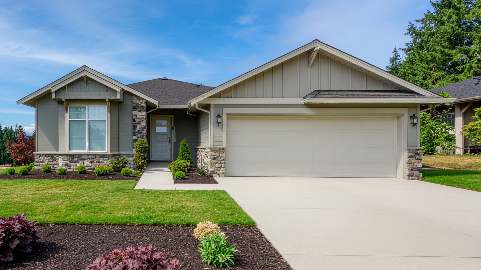Beige and stone ranch-style house with a two-car garage, green lawn, and blue sky.