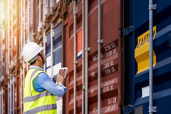 A man in a hard hat is standing next to a shipping container.