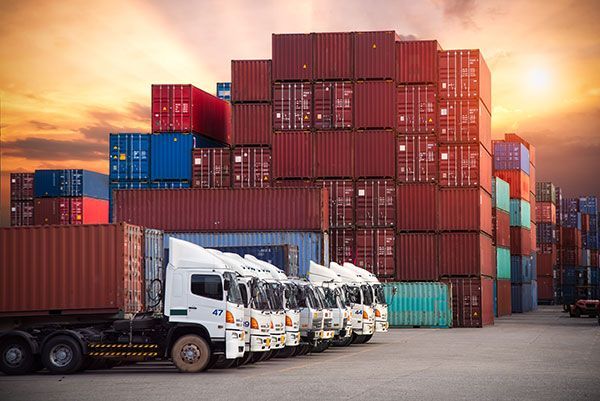 A row of trucks are parked in front of a stack of shipping containers.