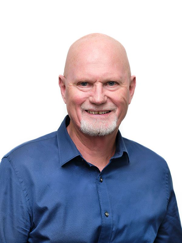 A bald man with a beard is wearing a blue shirt and smiling.