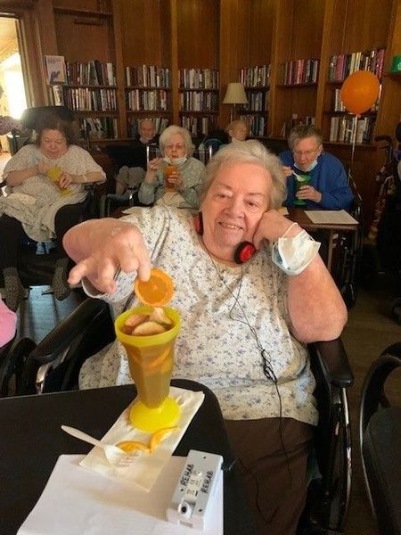 Group of seniors in a library, one woman holding a drink with an orange slice, smiling.