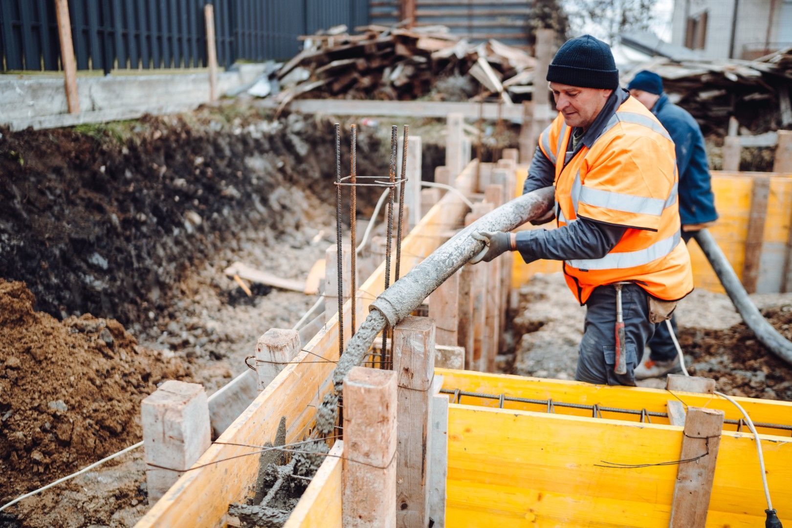 Construction worker pouring concrete into formwork on a construction site, wearing an orange vest.
