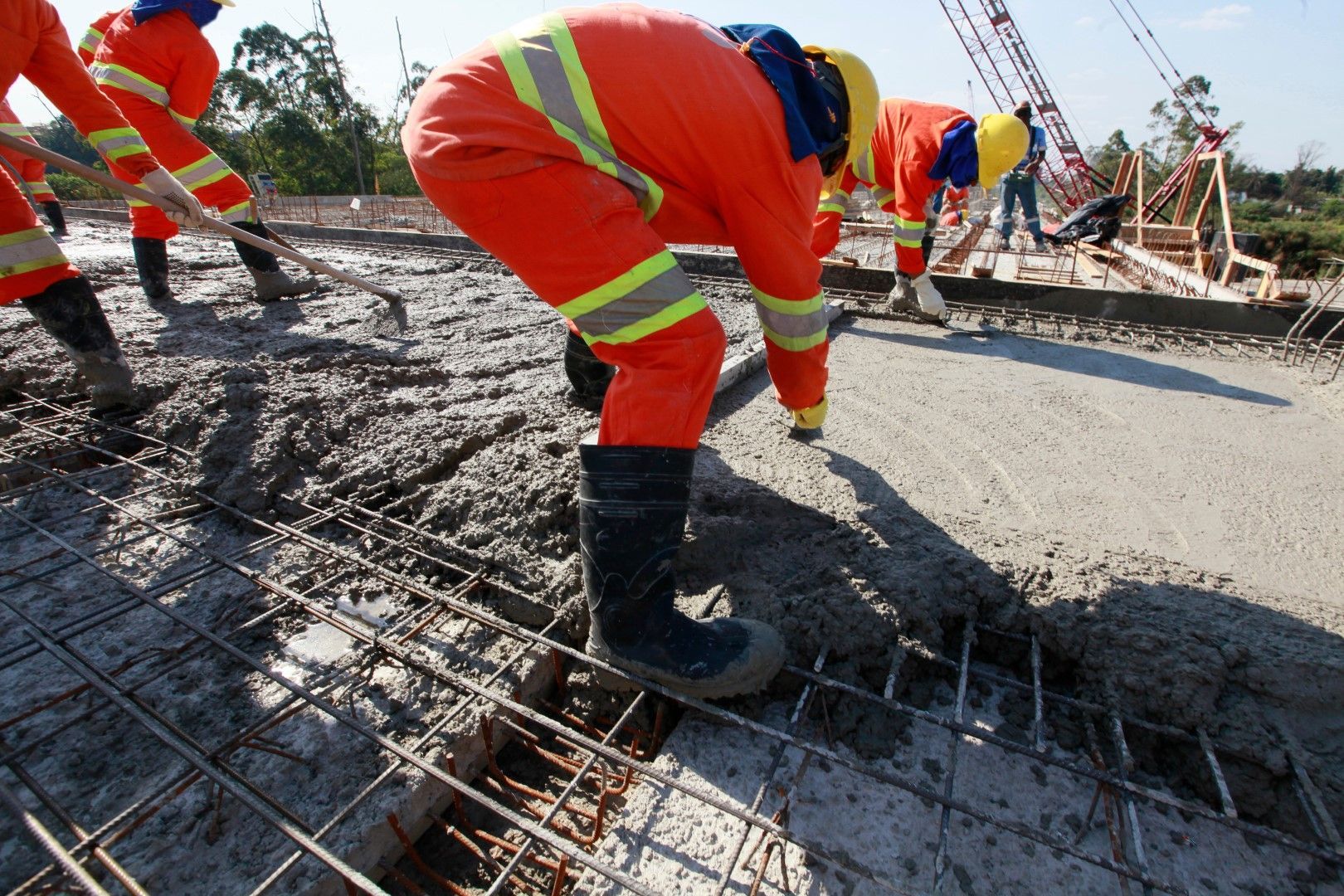 Construction workers in orange safety suits pouring concrete on a reinforced steel structure.