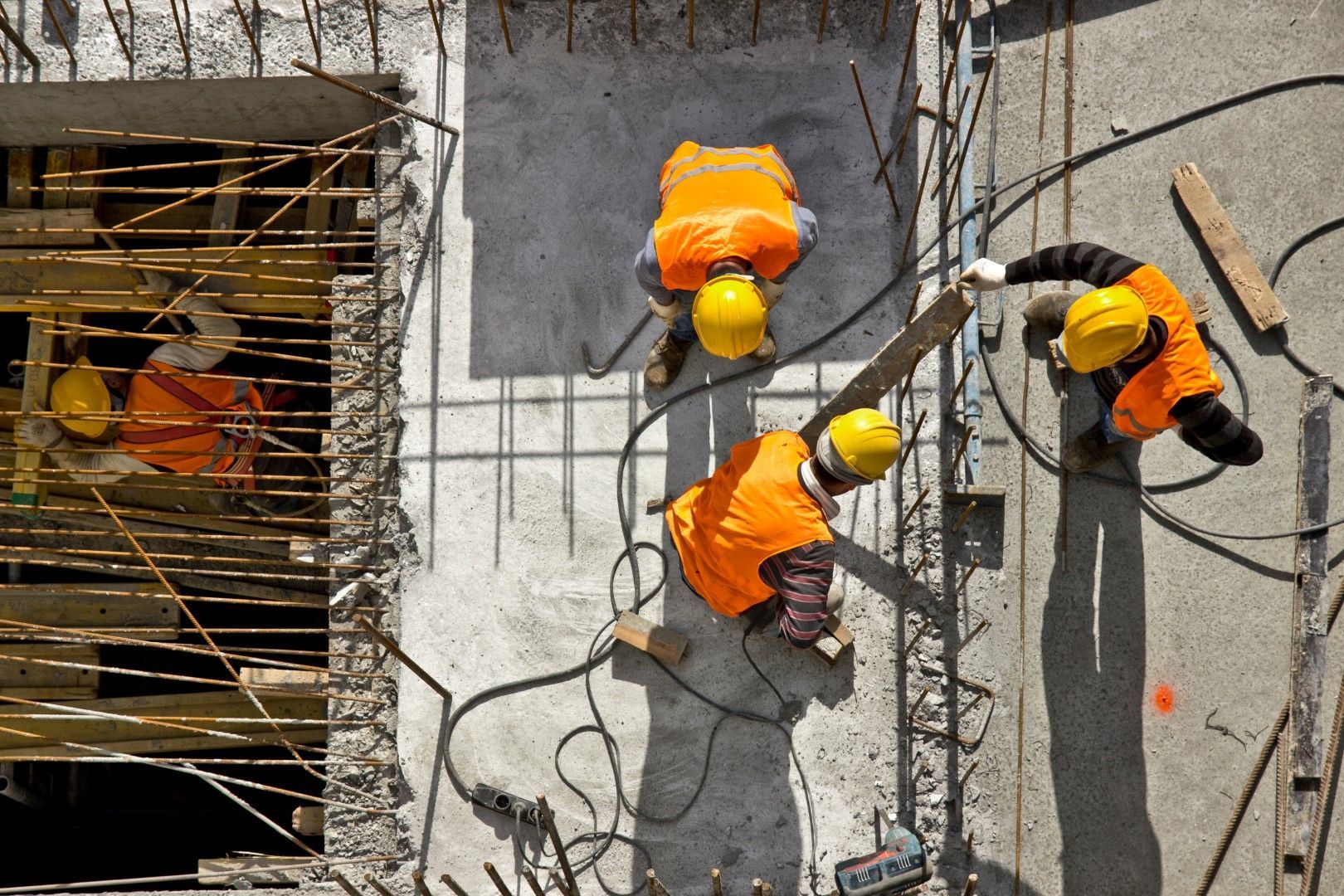 Construction workers wearing yellow helmets and vests working on a concrete structure.
