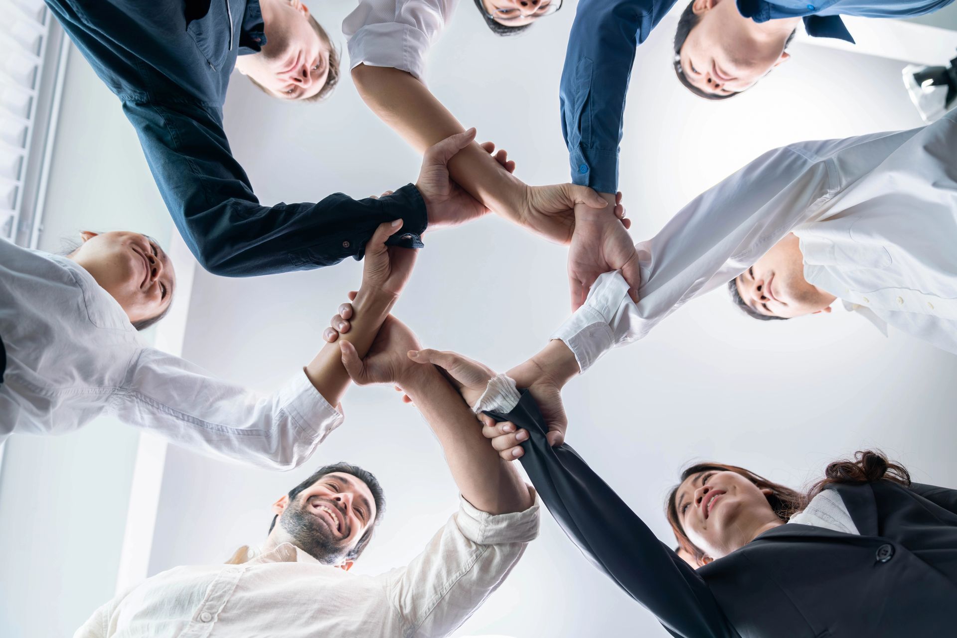 People holding hands in a circle, viewed from below, symbolizing teamwork and unity.
