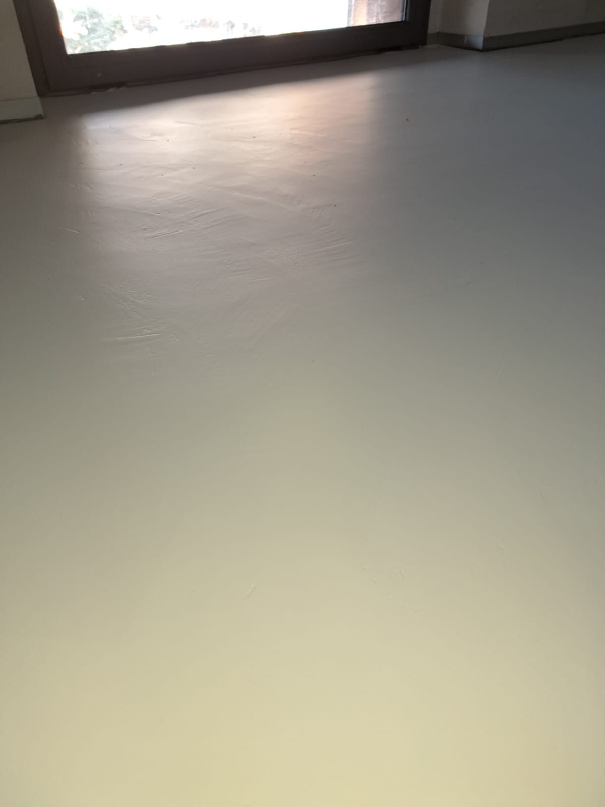 Pavimento grigio chiaro con luce solare proveniente da una finestra in alto.