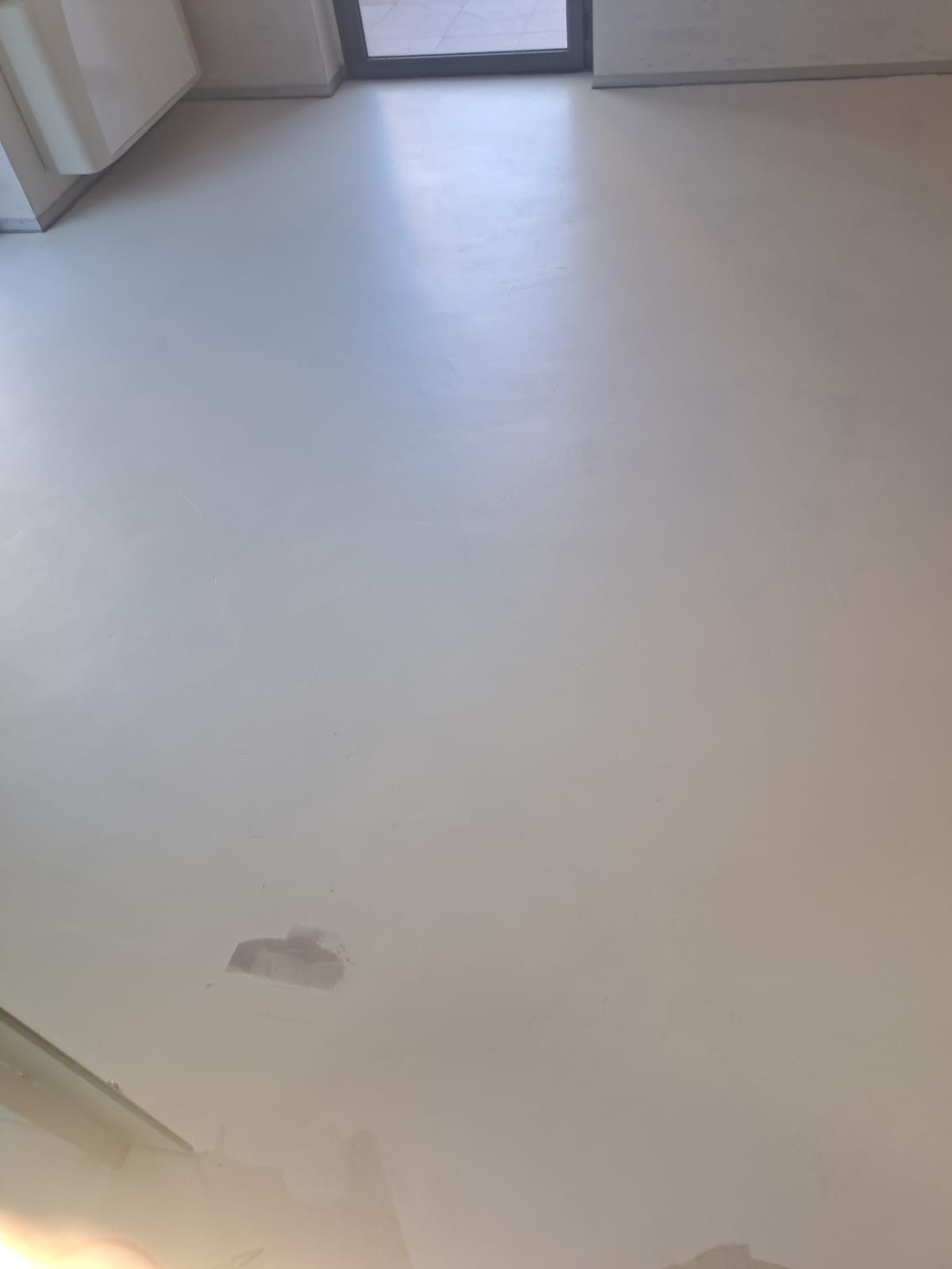 Pavimento bianco con una macchia più chiara al centro e una porta in lontananza.