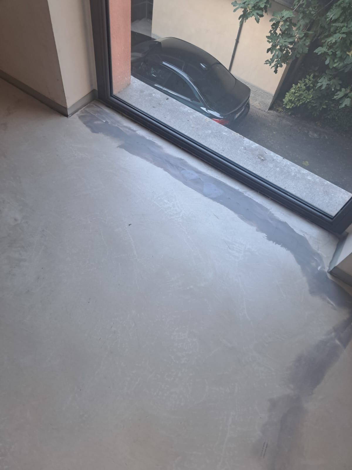 Pavimento grigio chiaro vicino a una porta scorrevole in vetro, con un'auto scura parcheggiata fuori.