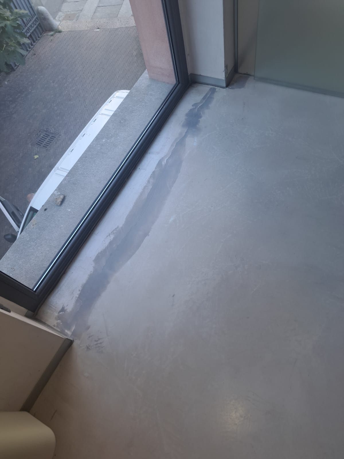 L'acqua si è accumulata sul pavimento grigio chiaro vicino a una finestra e a un telaio, probabilmente a causa di una perdita.
