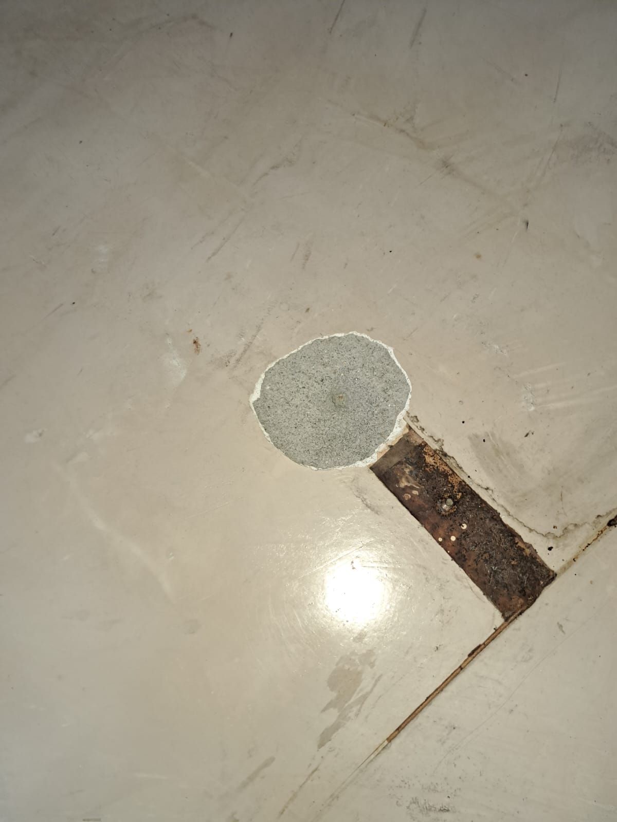 Pavimento bianco con una zona circolare rattoppata e una crepa lineare marrone scuro.