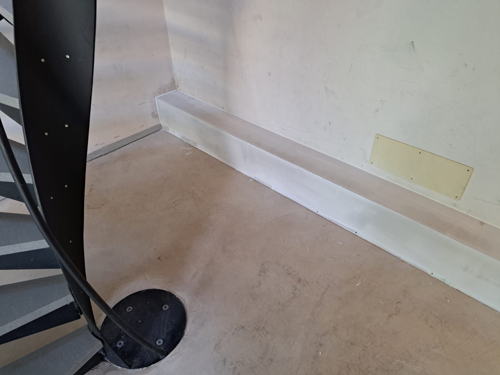 Scala a chiocciola con ringhiera nera e parete bianca, con battiscopa.