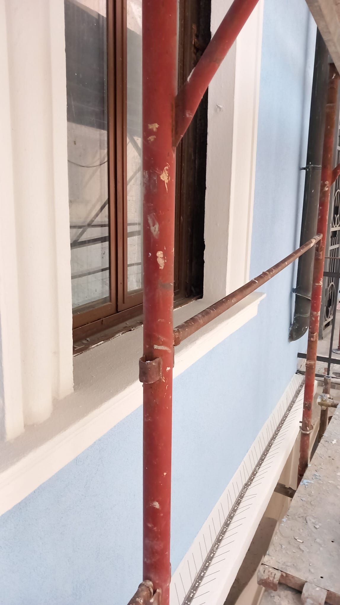 Impalcatura lungo un edificio con un muro blu, finiture bianche e una finestra.