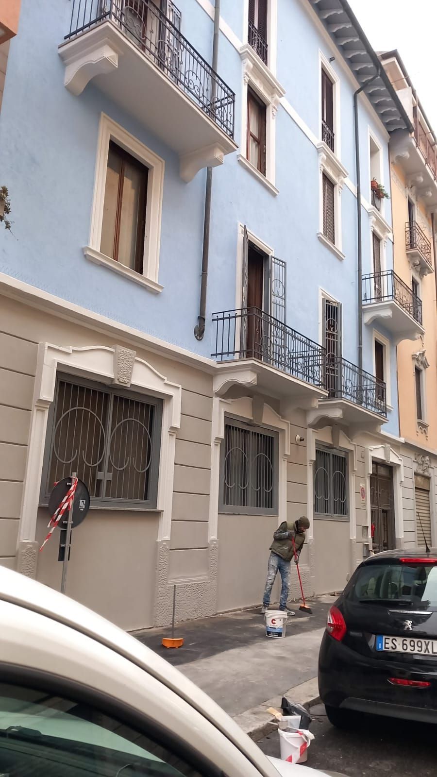 Uomo che dipinge il muro esterno di un edificio blu in una strada cittadina.