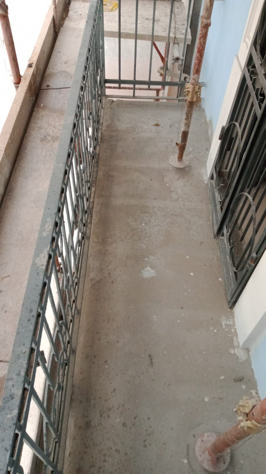 Balcone stretto con pavimento in cemento, ringhiera in metallo e impalcature.