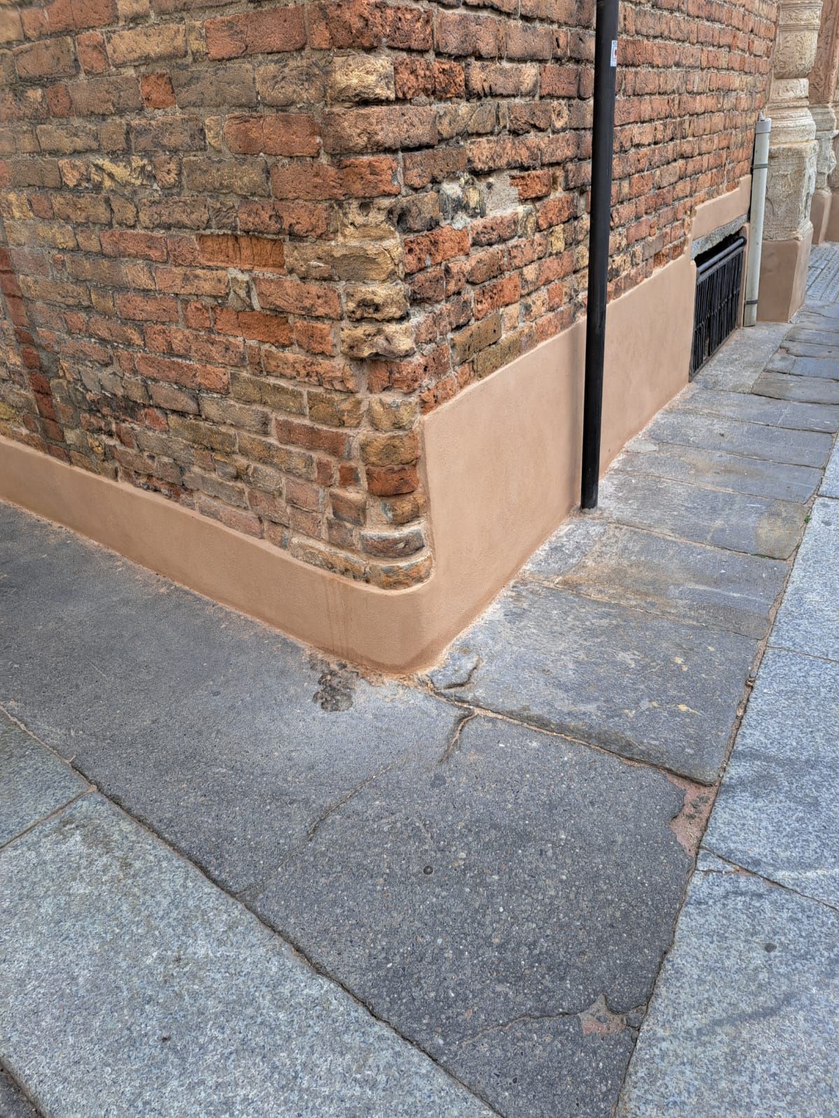 Angolo di un edificio in mattoni con base appena intonacata; marciapiede in primo piano.