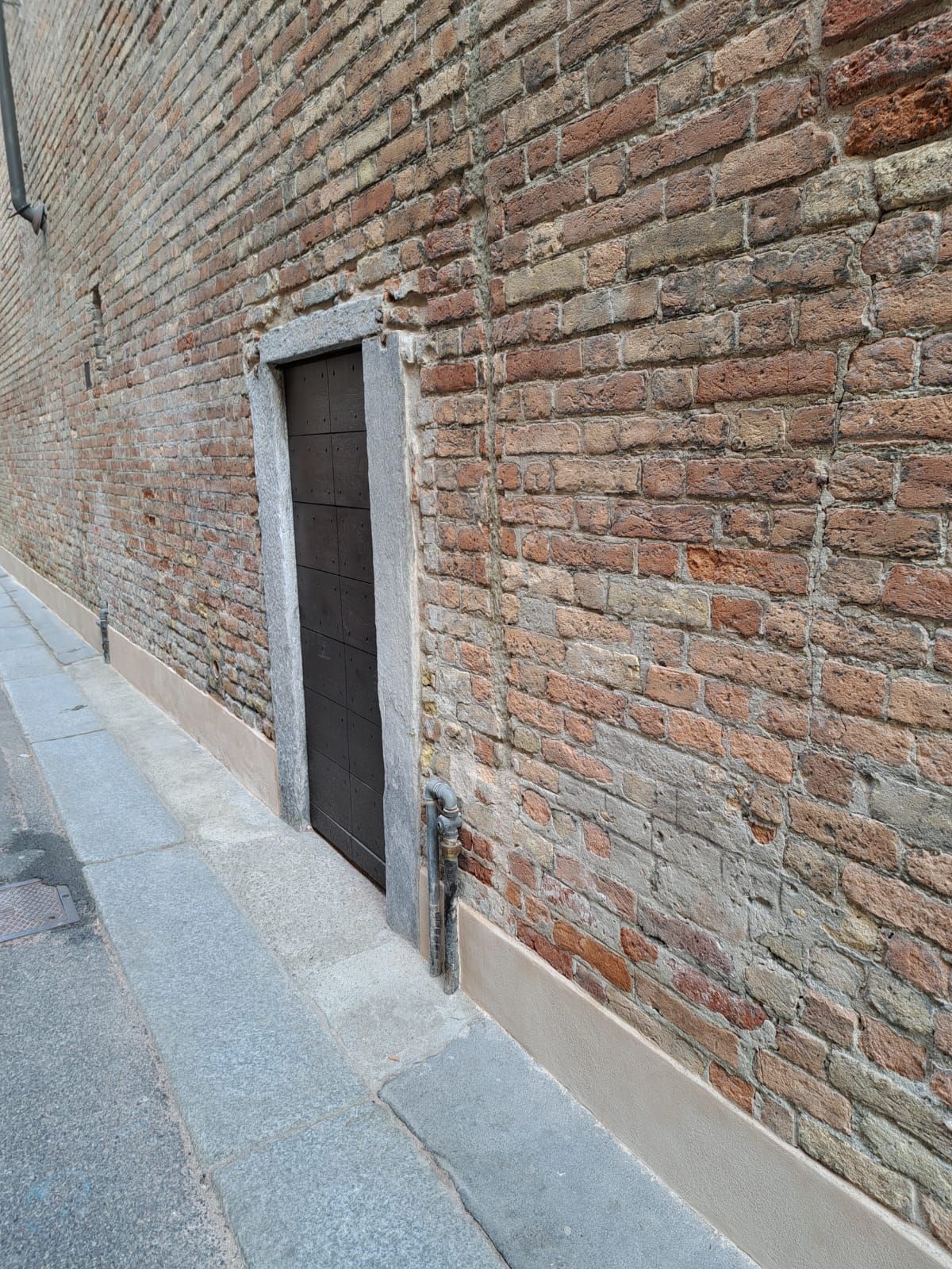 Muro di mattoni con porta arretrata, marciapiede sulla sinistra.