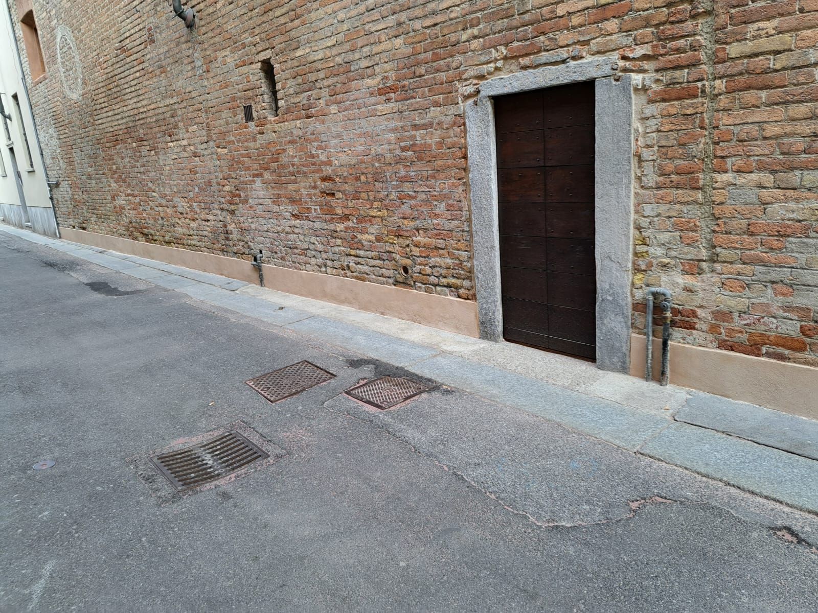 Edificio in mattoni con una porta di legno scuro, accanto a una strada lastricata di grigio.
