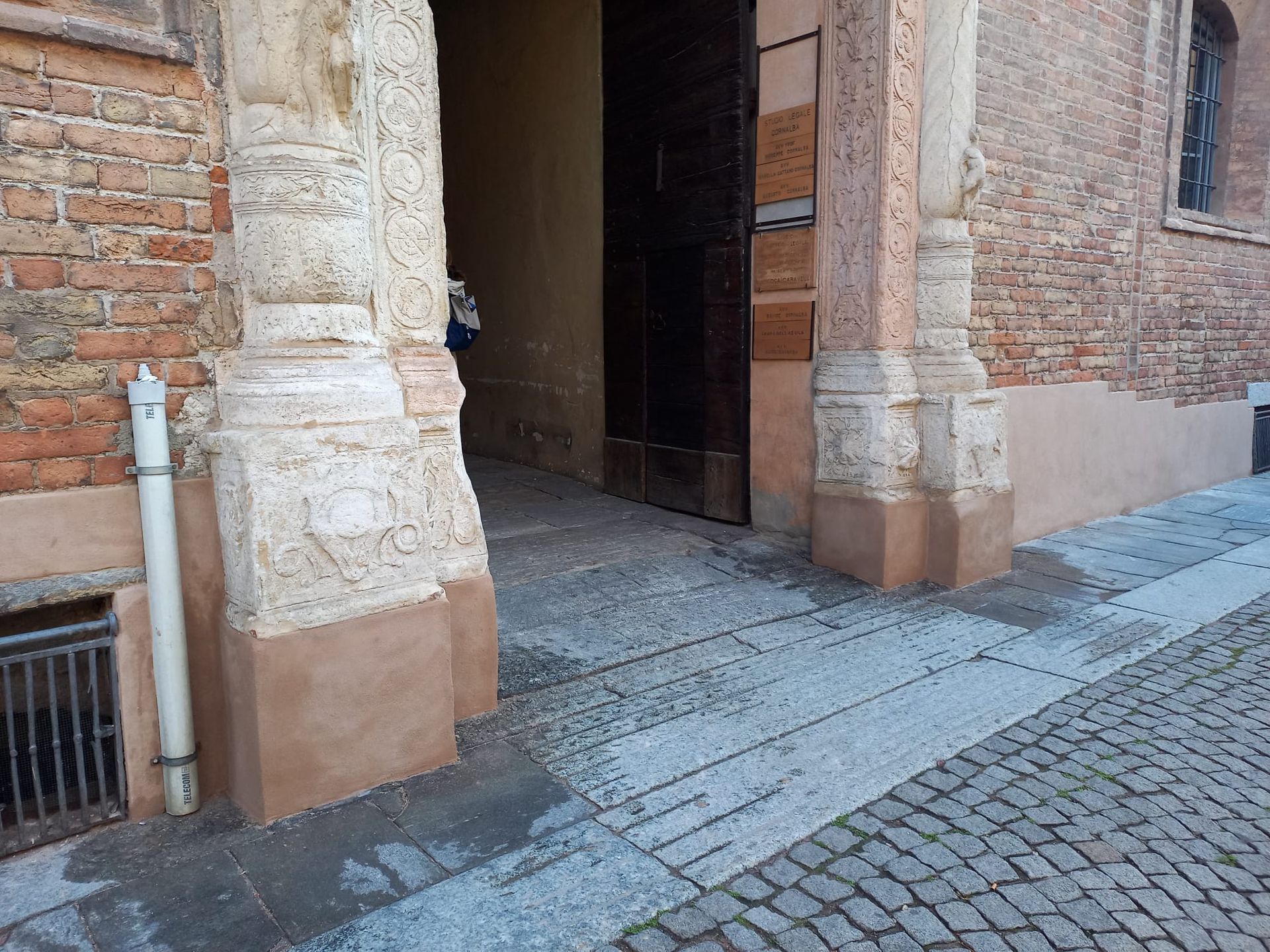 Esterno di un edificio in mattoni con colonne e un portale; pavimentazione in ciottoli.