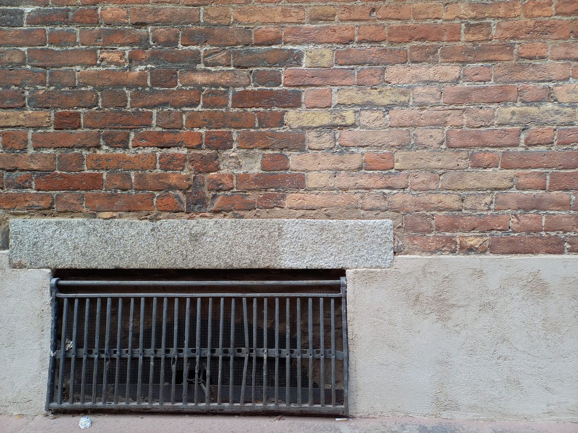 Muro di mattoni con una grata metallica sul fondo, probabilmente una finestra del seminterrato.
