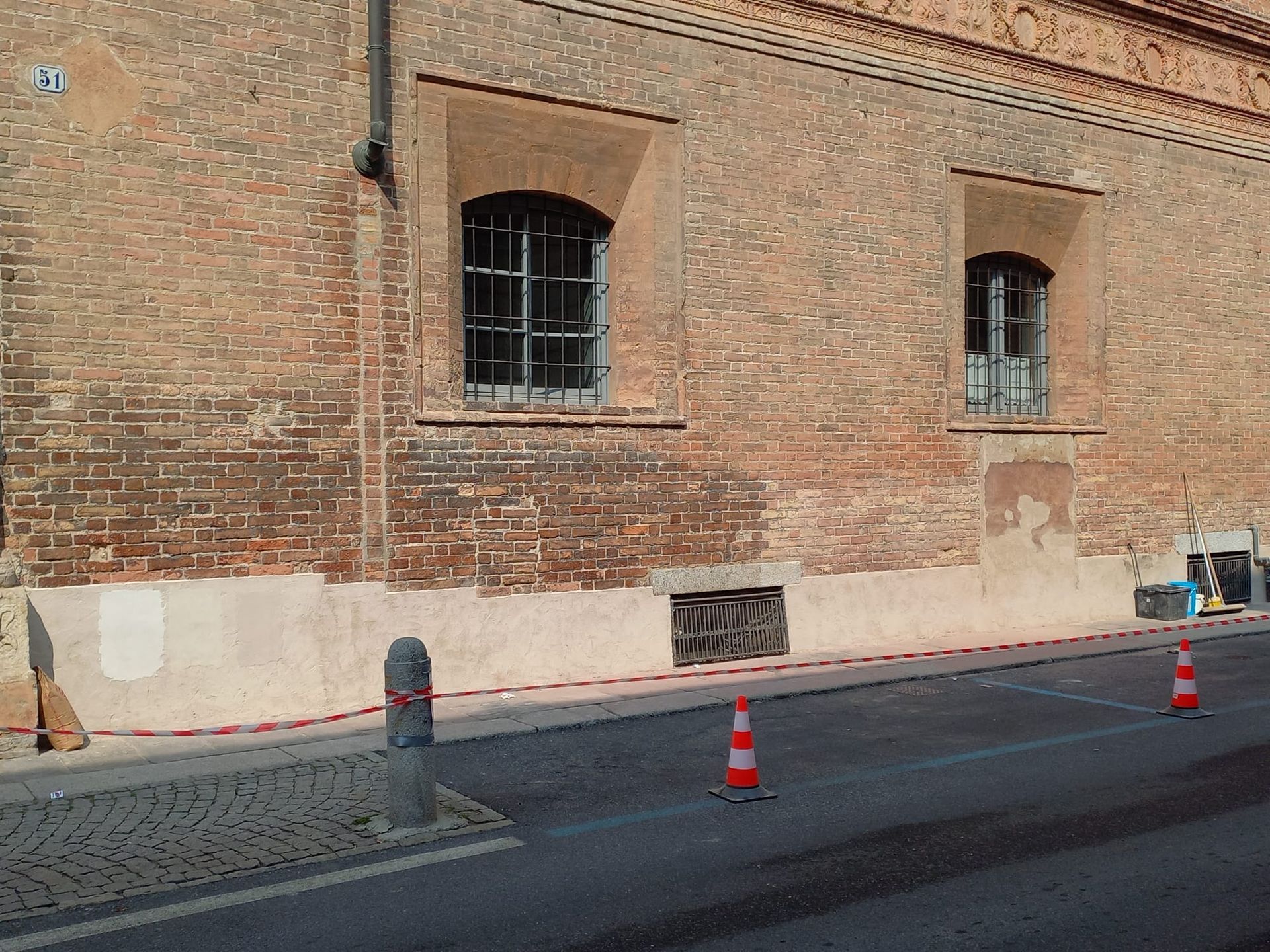 Edificio in mattoni con due finestre ad arco, una strada e coni stradali.