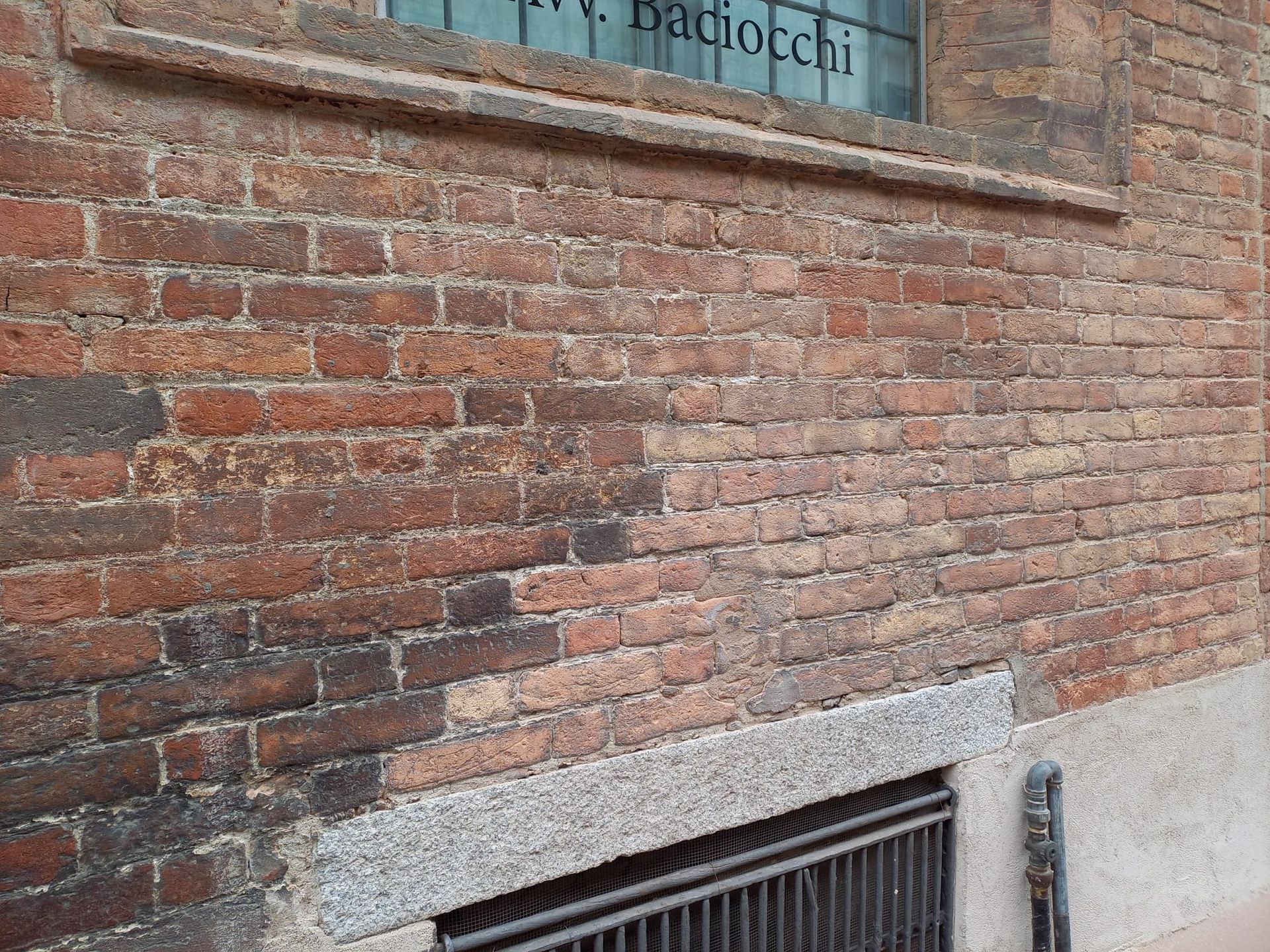 Muro di mattoni con colorazione scura, vicino a una finestra con il nome