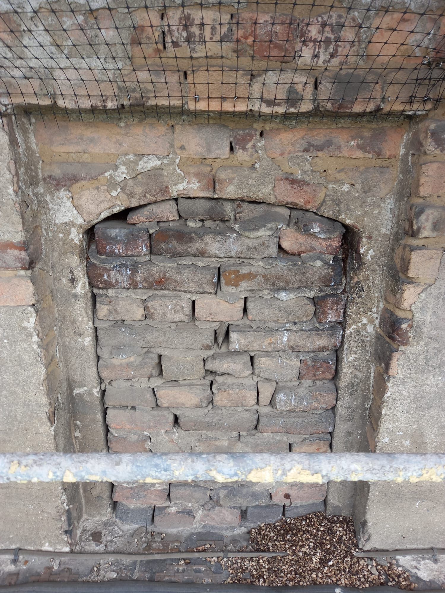 Apertura ad arco murata in un muro di mattoni, forse un camino. Mattoni marroni, malta grigia.