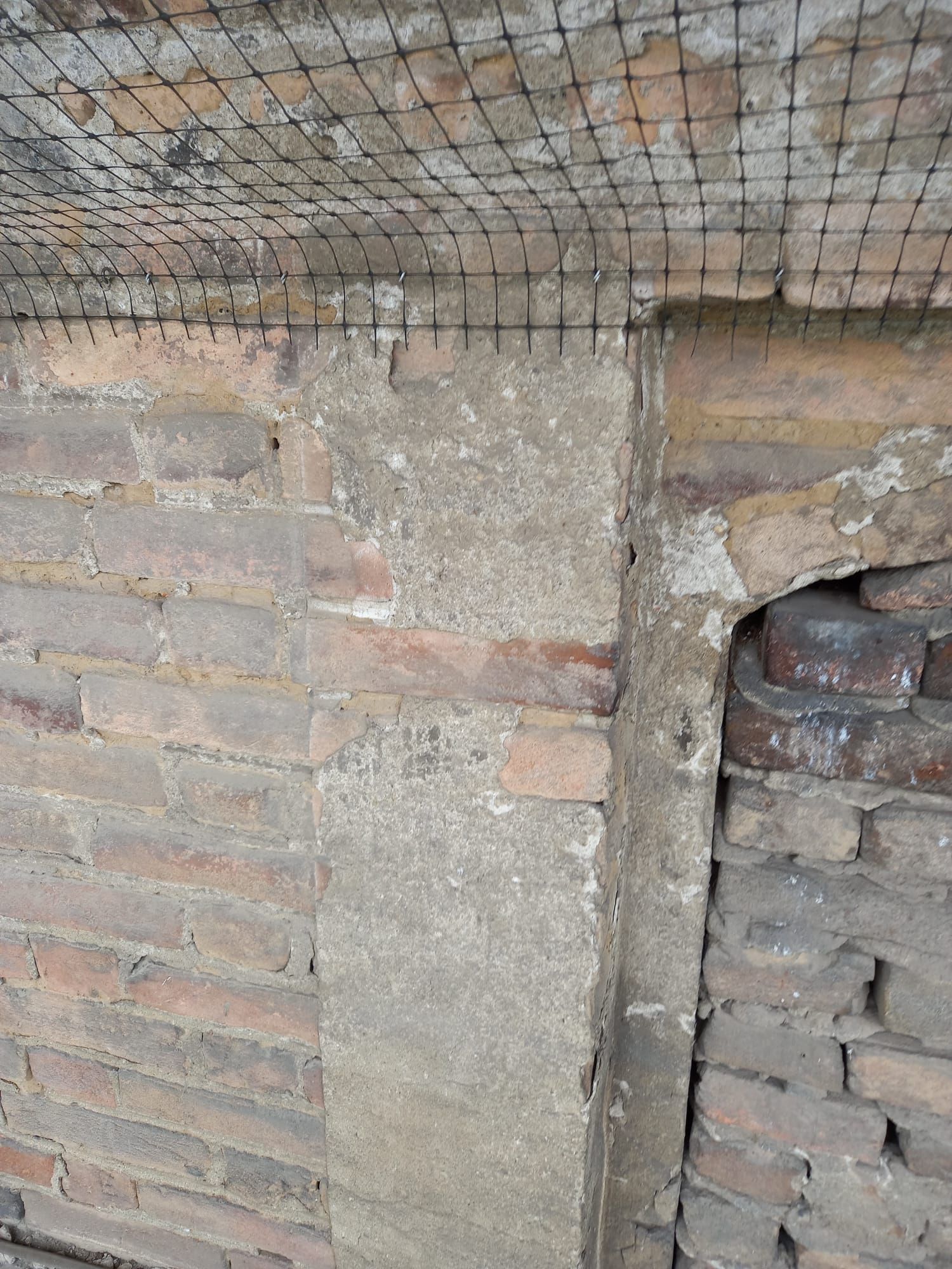 Muro di mattoni con un pilastro di cemento e una rete metallica sul soffitto.