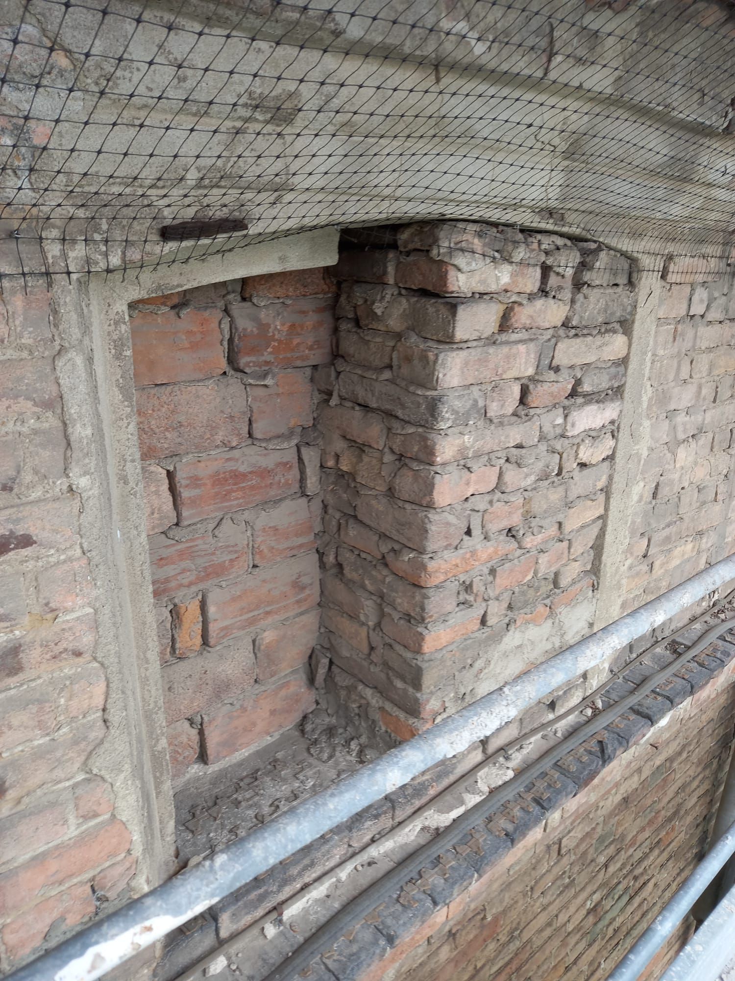 Finestra murata in un muro di mattoni con malta visibile e rete metallica di rinforzo sopra.