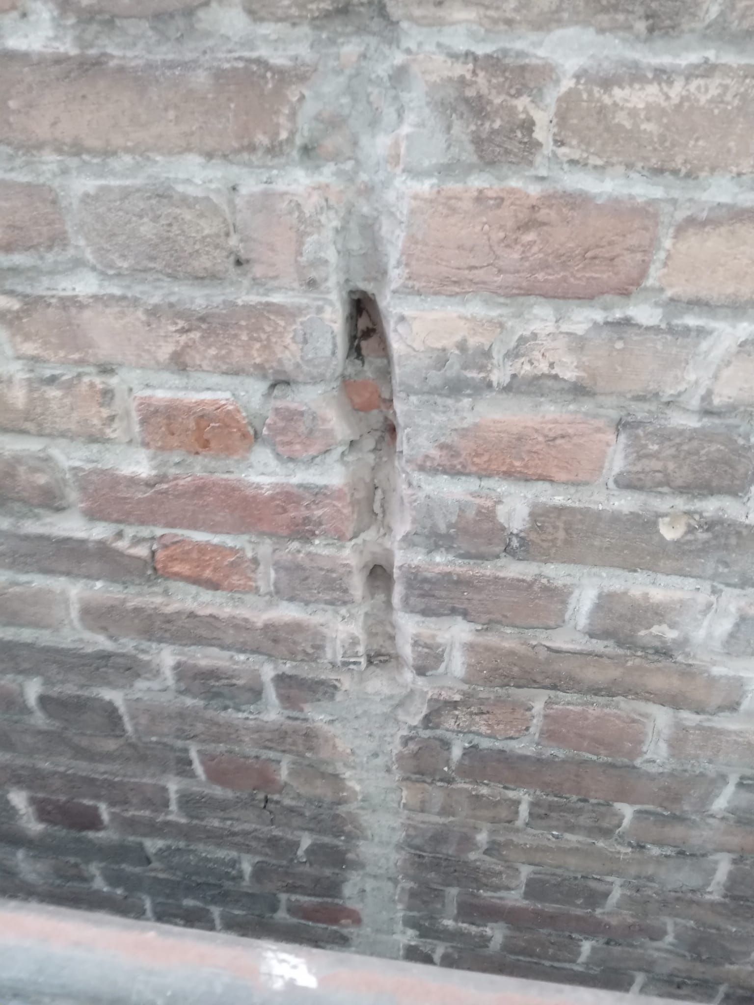 Muro di mattoni con una crepa verticale riempita di malta.