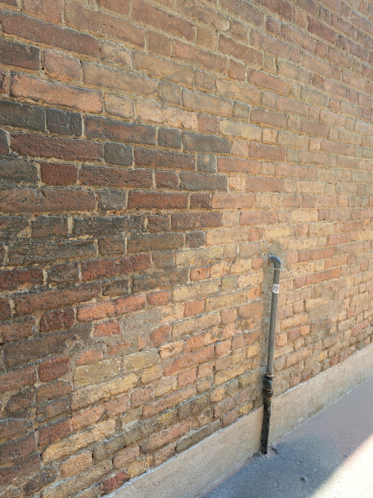 Muro di mattoni con un tubo che si estende verso l'alto, ombreggiato dalla luce del sole.