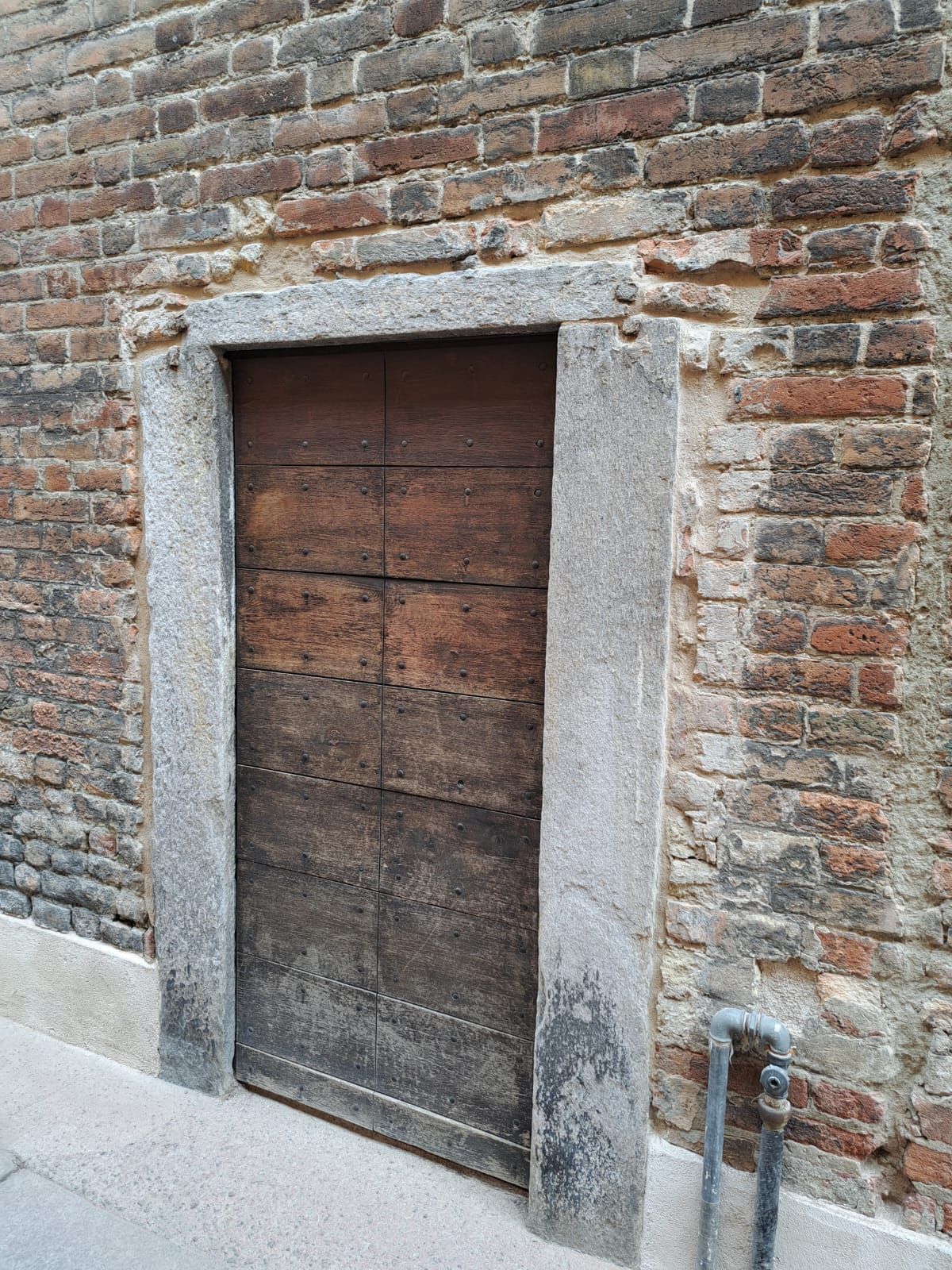 Porta di legno con cornice in pietra incastonata in un muro di mattoni.