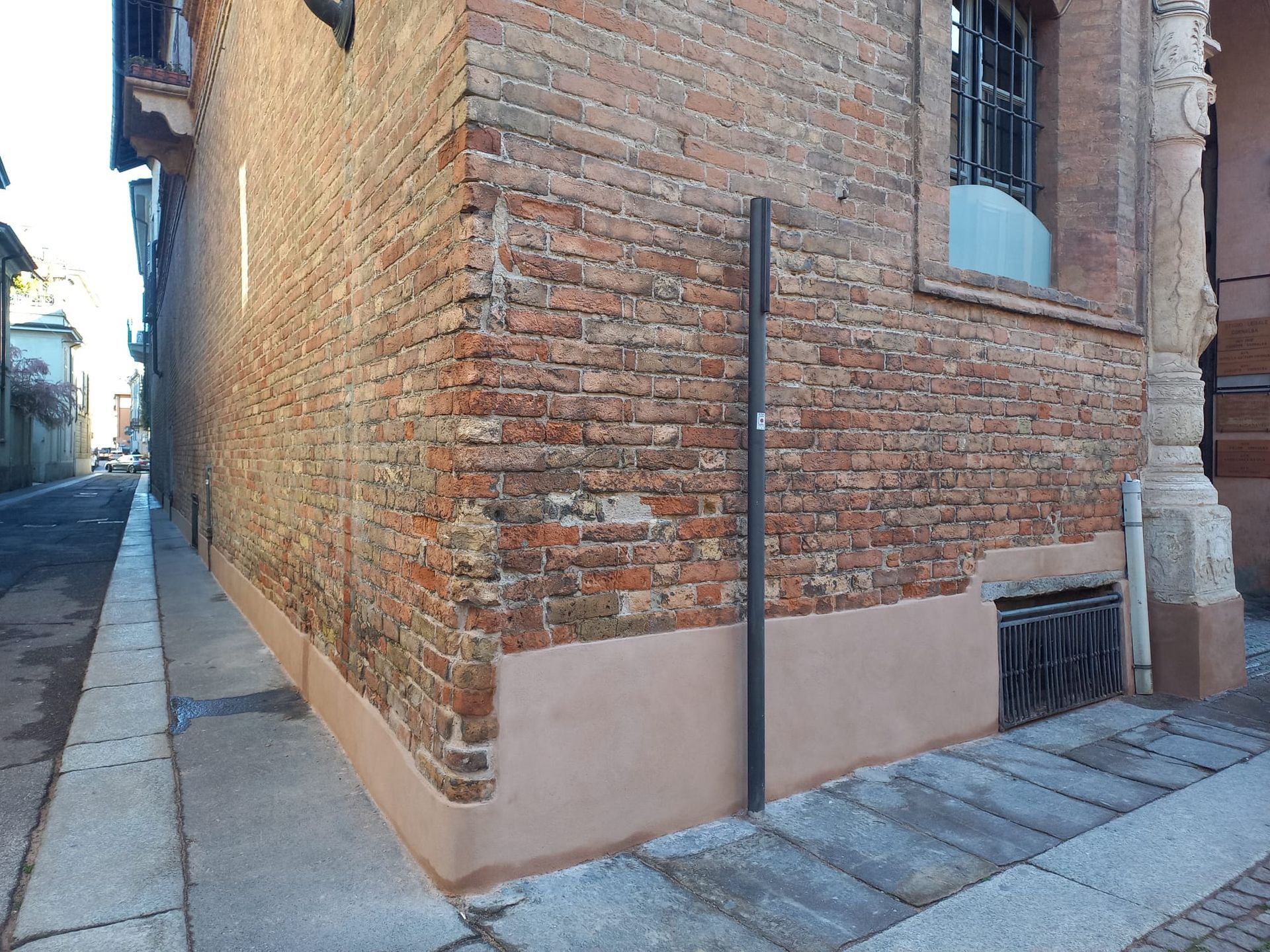 Angolo di un edificio in mattoni, strada stretta. Muro in mattoni rossi con la parte inferiore dipinta di marrone chiaro.