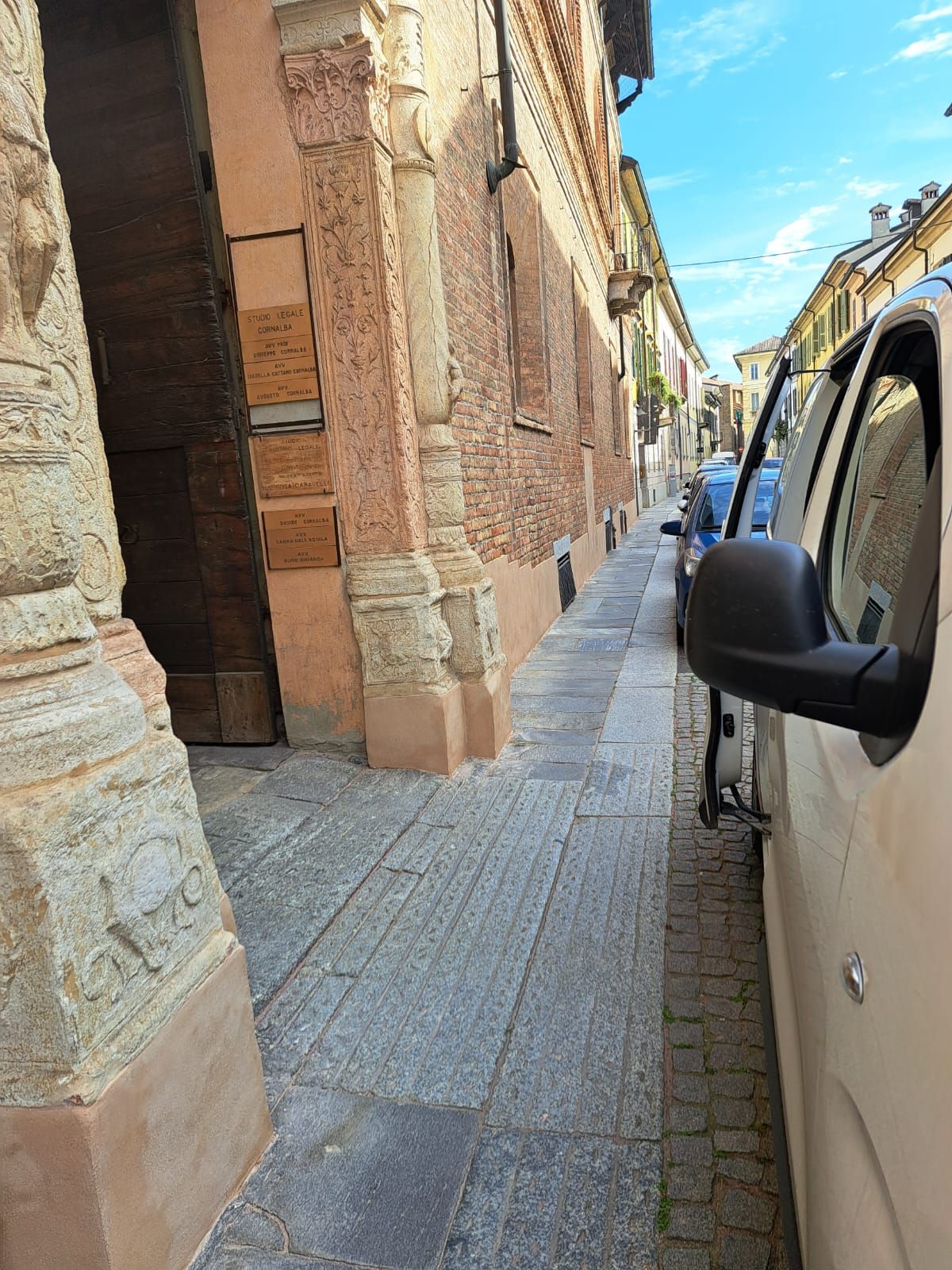 Stretta strada acciottolata con edifici in mattoni e un furgone parcheggiato.