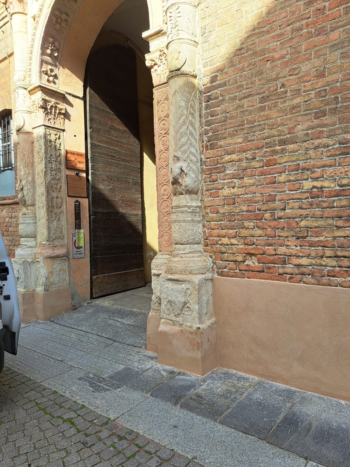 Arco d'ingresso con colonne in pietra, muro in mattoni rossi, grandi porte in legno. Giornata di sole.