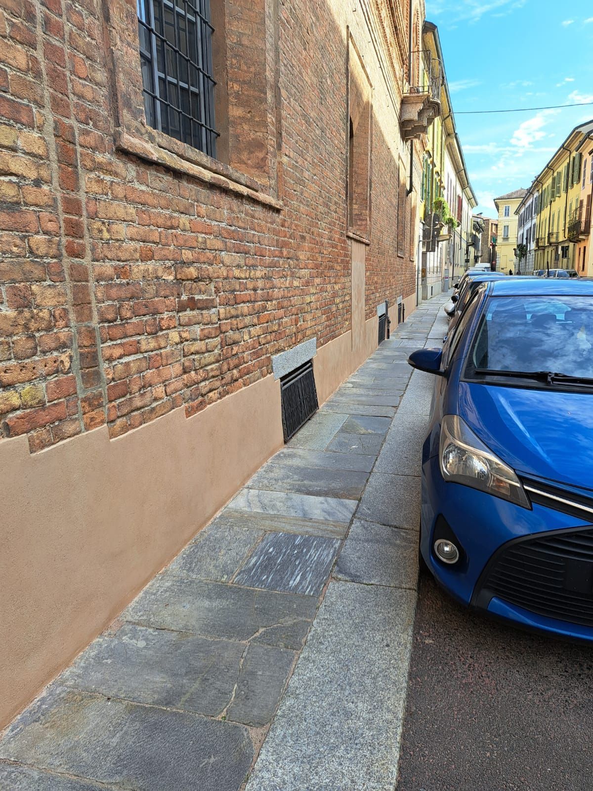 Uno stretto muro di mattoni con un'auto blu parcheggiata sul ciglio della strada.