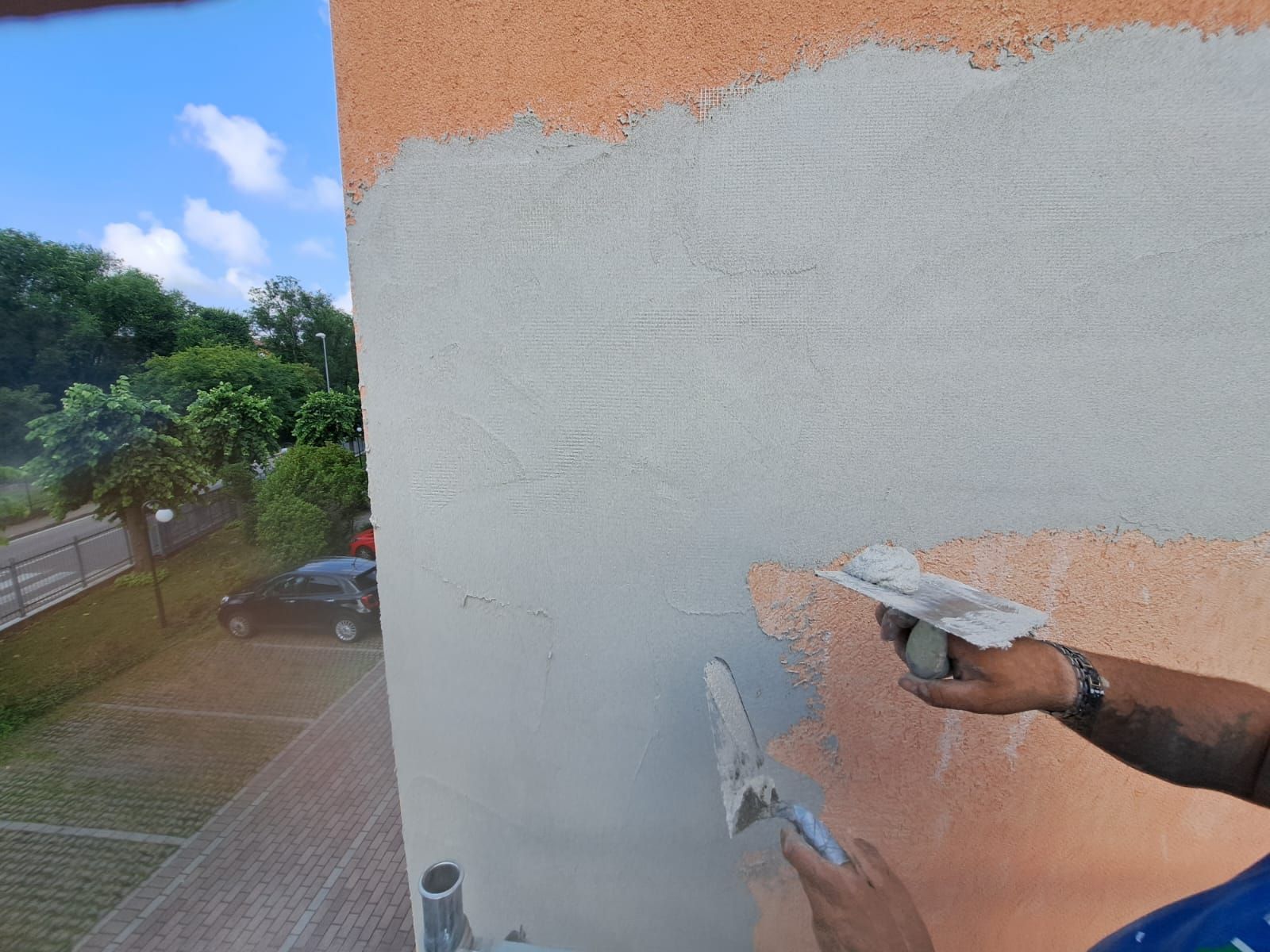 Uomo che applica stucco grigio con una cazzuola sulla facciata di un edificio.