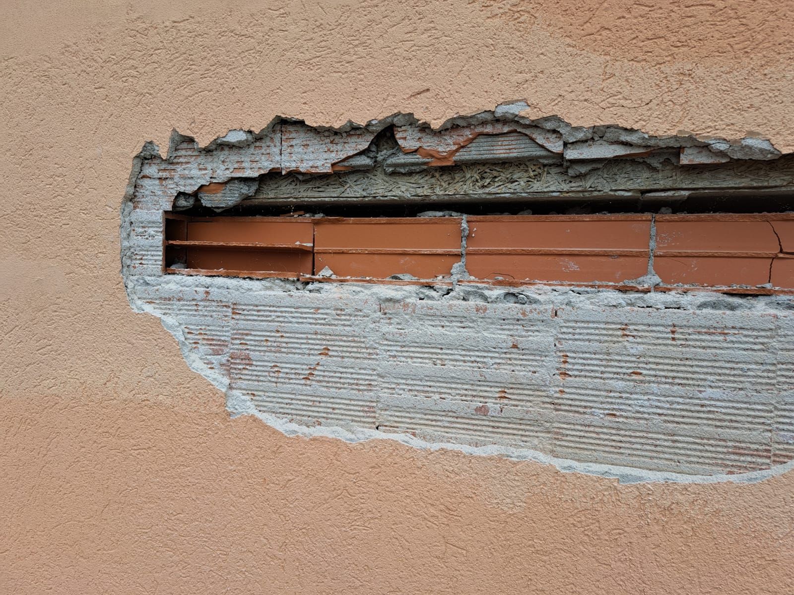 Buco in un muro dipinto di arancione che rivela mattoni e malta grigia; esterno.