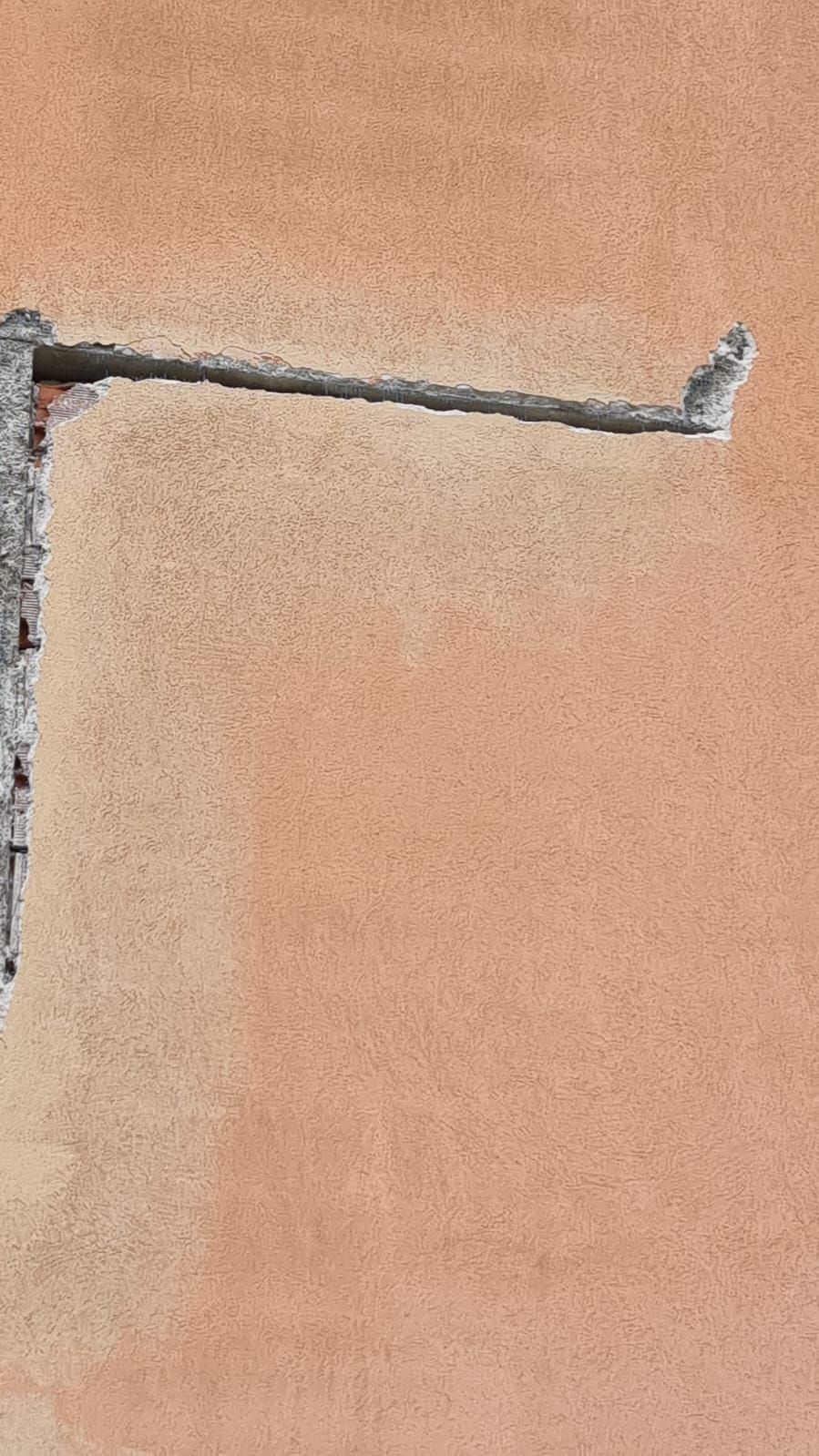 Muro color pesca danneggiato con una crepa orizzontale che si estende dal bordo sinistro.