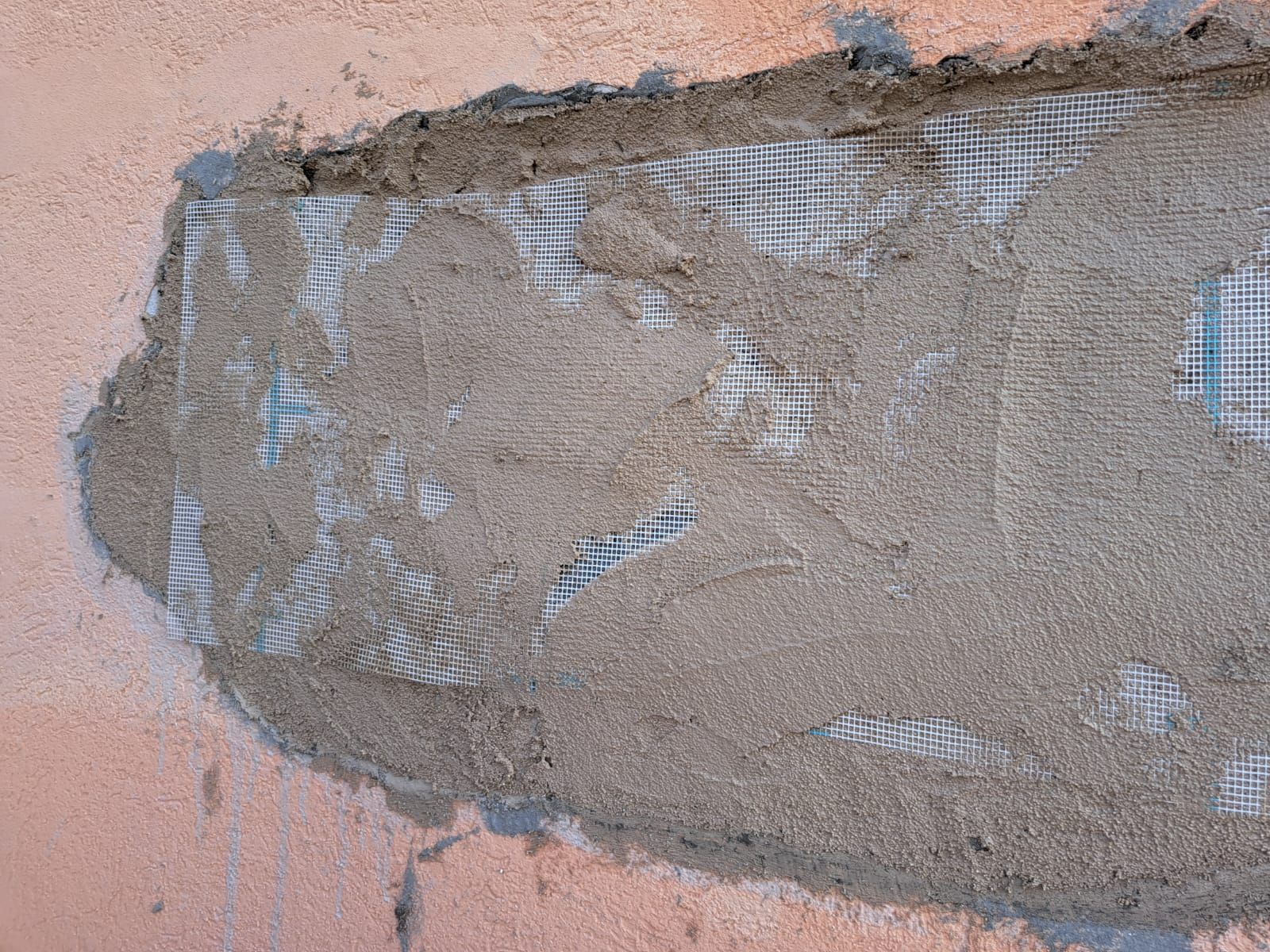 Pezzo di cemento su un muro esterno rosa, che rivela la rete di rinforzo.