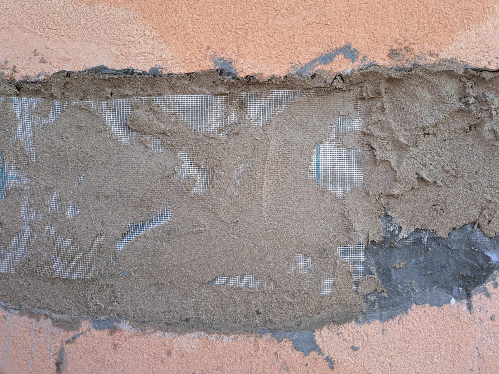 Cemento e rete applicati a un muro di mattoni per ripararne una sezione.