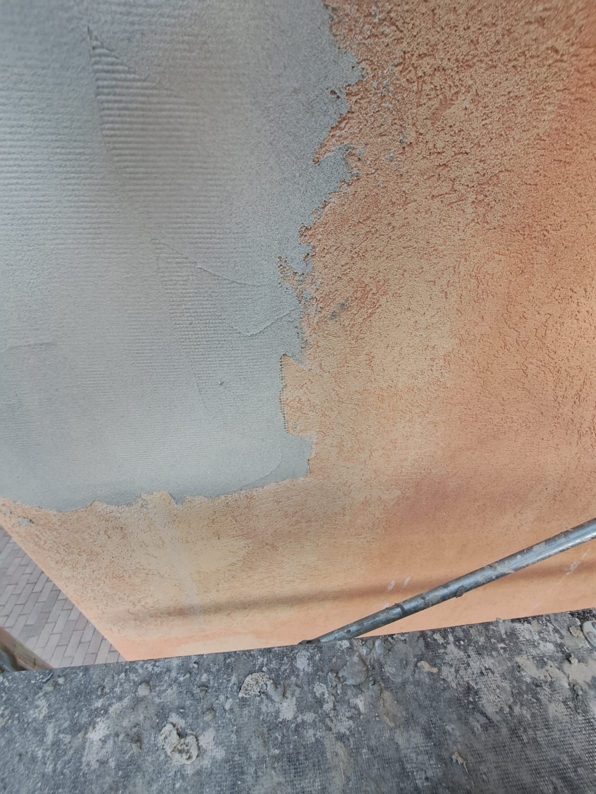 Soffitto semi-coperto con materiale grigio, adiacente a una sezione esposta color arancio-marrone. È visibile un'asta metallica.