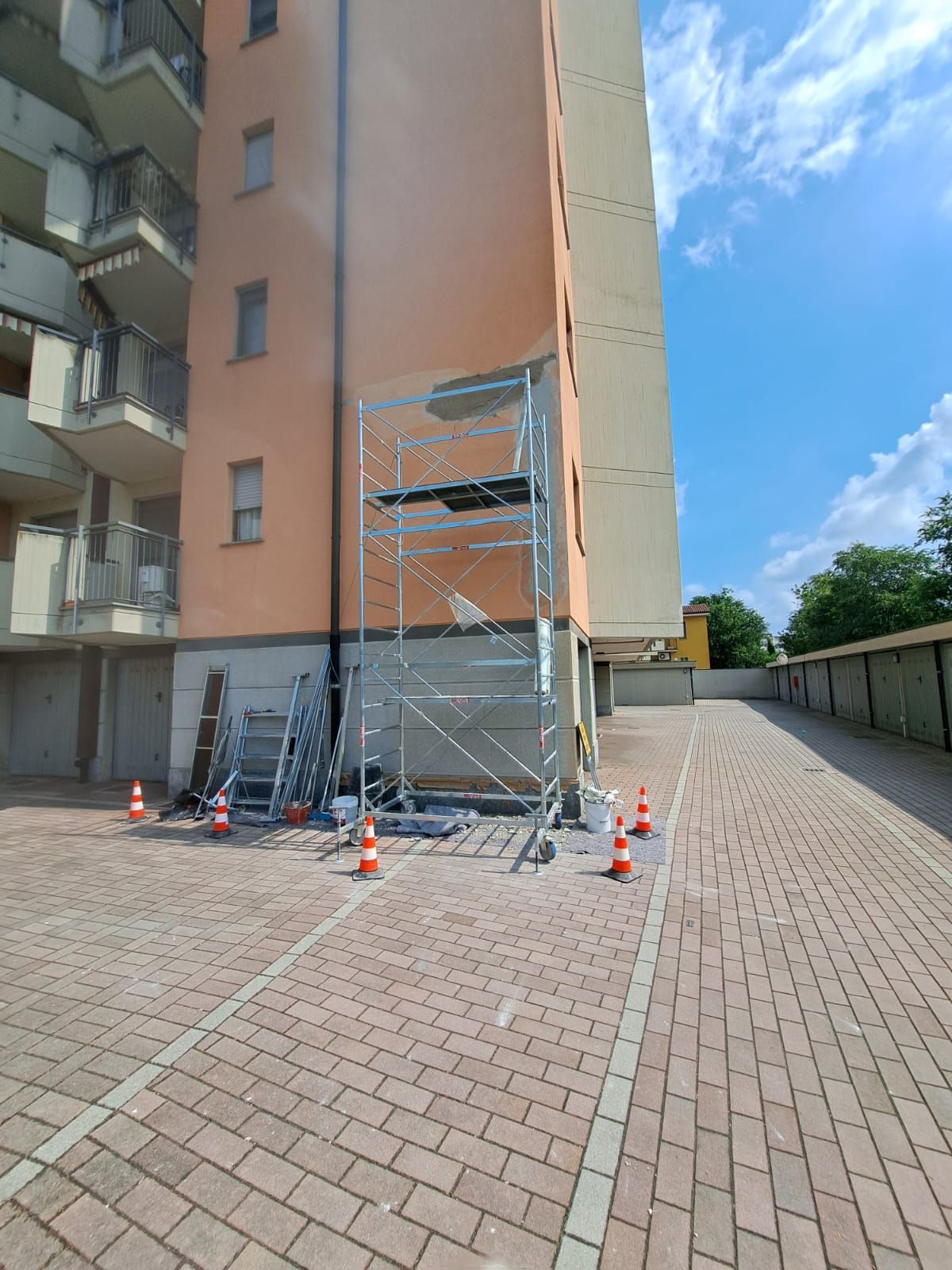 Impalcature installate contro un alto edificio per lavori esterni, con coni arancioni che delimitano il terreno.