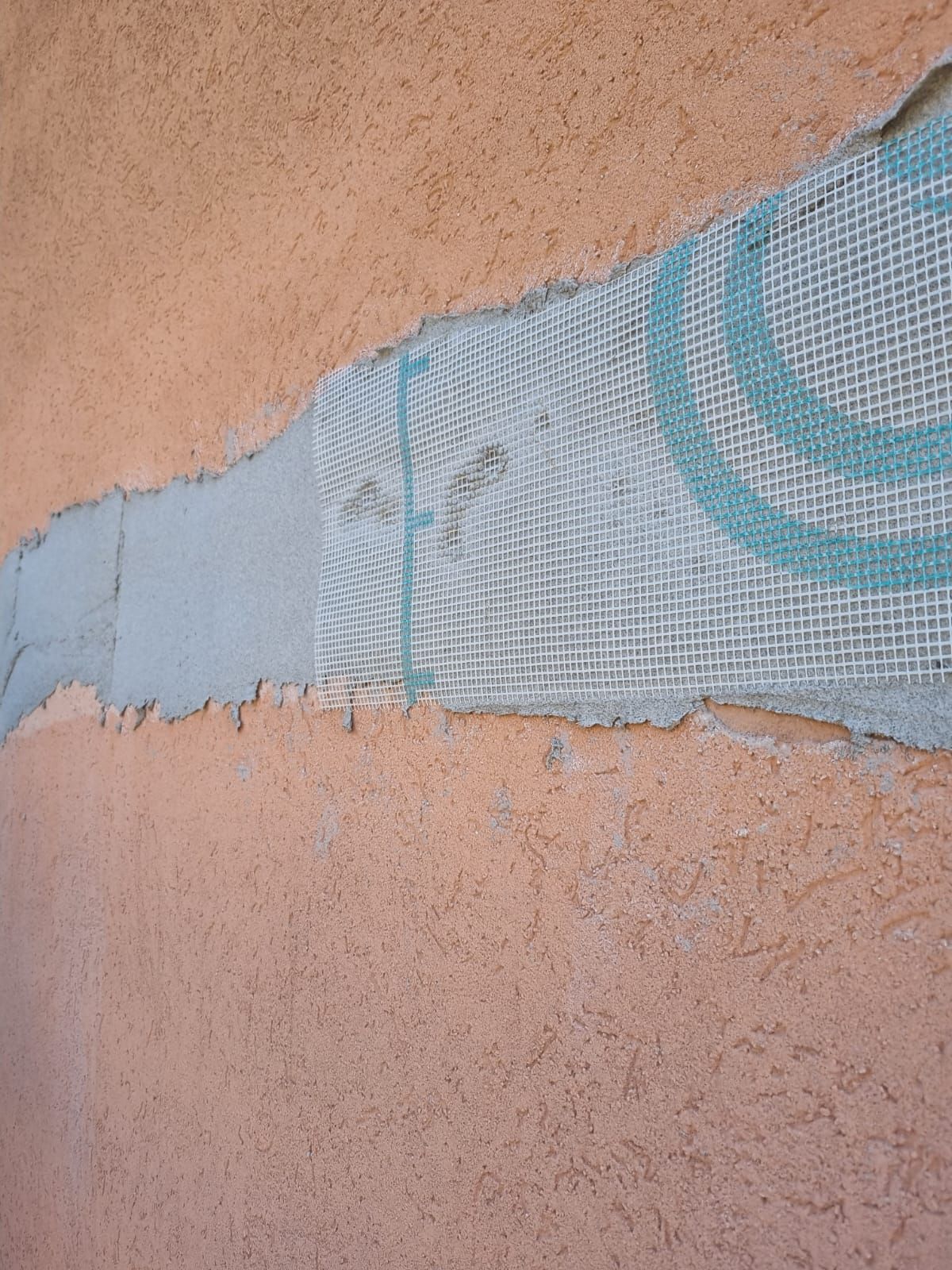 Parete in stucco danneggiata che rivela un rinforzo in rete bianca.