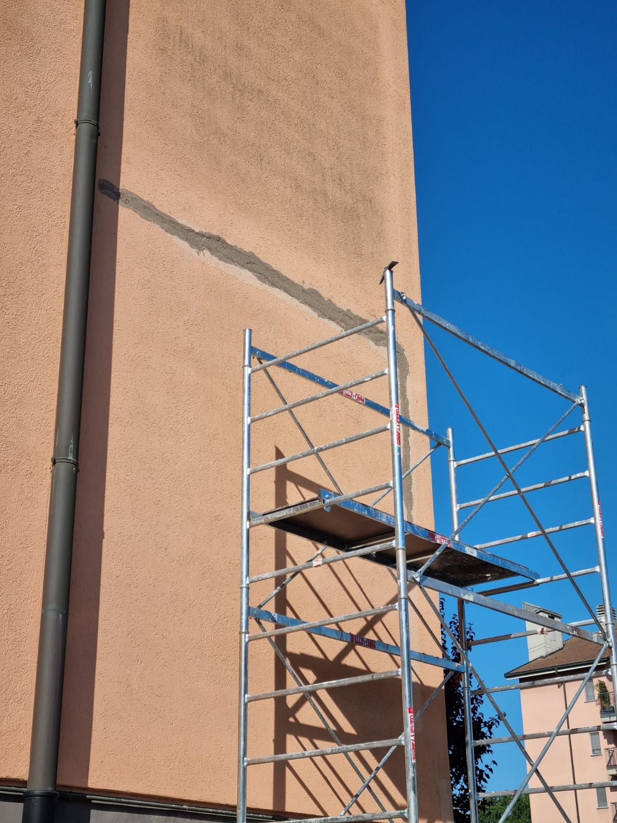 Impalcatura accanto a un edificio con una crepa verticale riparata; cielo azzurro e limpido.