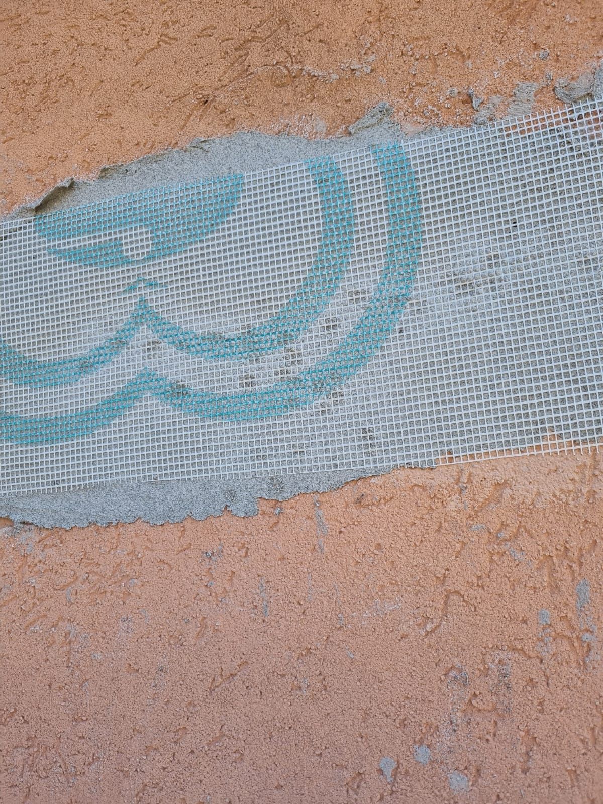 Frammento di tessuto con motivo azzurro su parete arancione consumata dal tempo.