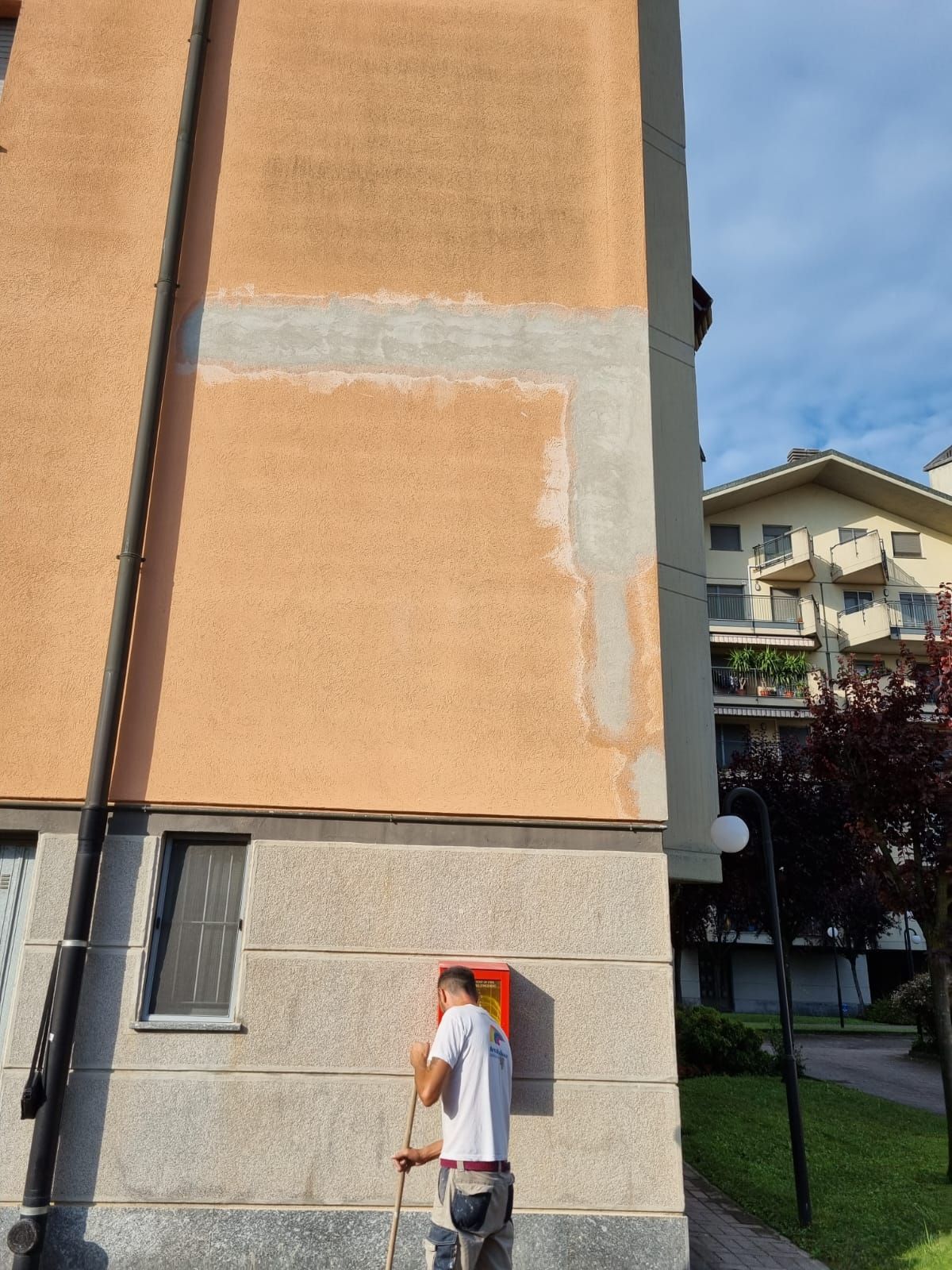 Uomo che dipinge l'esterno di un edificio arancione; è visibile una macchia di vernice mancante.